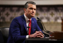 Pentagon Chief SLAMMED—Where’s the Endgame? Man in blue suit speaking at a microphone
