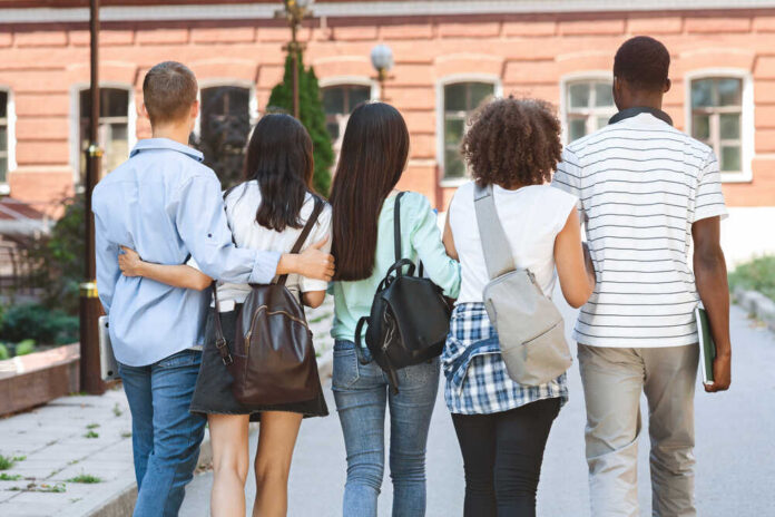 College,Friendship.,Group,Of,Five,Students,With,Backpacks,Walking,At Statue in front of a grand state capitol building on a winter day