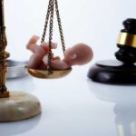 Scales of justice with a small baby figurine on one side and a gavel in the background