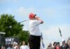 A golfer in a red cap swings a golf club at an outdoor event