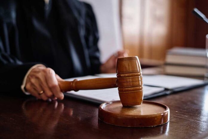Judge,Of,Supreme,Court,Hitting,Sounding,Block,With,Wooden,Gavel A judge's hand holding a gavel in a courtroom setting