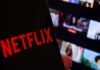 Close-up of a smartphone displaying the Netflix logo with a blurred background of movie thumbnails