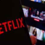 Close-up of a smartphone displaying the Netflix logo with a blurred background of movie thumbnails