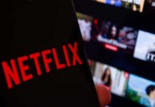 Close-up of a smartphone displaying the Netflix logo with a blurred background of movie thumbnails