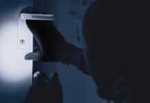 Tech-Savvy Burglars Exploit Social Media Clues A gloved hand attempting to unlock a door in low light