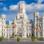 A grand historic building with flags in front and a fountain