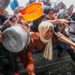 Drone Assault Turns Soup Kitchen Into Bloodbath women and children reach with pots at a crowded aid distribution