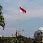 Indonesian flag waving in front of a building and palm trees