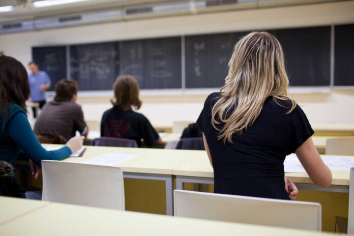 Young,Pretty,Female,College,Student,Sitting,In,A,Classroom,Full Students seated in a classroom listening to a teacher