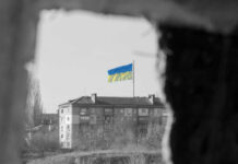 Hypersonic Chaos: Russia’s Unstoppable Kyiv Assault Ukraine flag on building seen through dark frame.