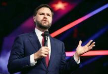 Vance’s Bold Stand: Anti-American Violence Slammed Man in suit speaking with microphone on stage.