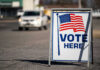 Election Integrity Battle: Will SAVE Act Prevail? Vote Here sign with American flag.