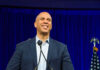 Party Panic: Booker Won’t Back Platner Man smiling at podium with American flag behind