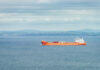 Orange cargo ship sailing on calm sea with distant green hills