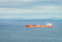 Orange cargo ship sailing on calm sea with distant green hills