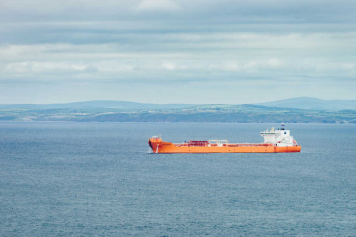 Orange cargo ship sailing on calm sea with distant green hills