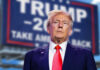 Trump’s AI Gambit Rattles Silicon Valley man in suit with red tie standing before a blurred campaign-style sign