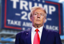 Trump’s AI Gambit Rattles Silicon Valley man in suit with red tie standing before a blurred campaign-style sign