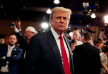 Media Spin Exposed: Trump-Zelensky Twist Man in a navy suit with red tie stands amid a crowded event