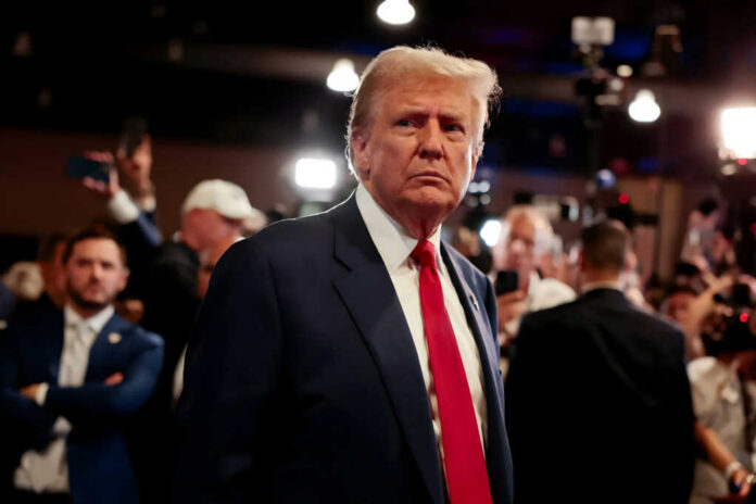 donald-trump2549626775jpg Man in a navy suit with red tie stands amid a crowded event