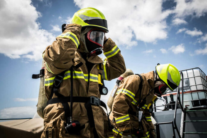 Firefighters in protective gear standing outside cloudy sky