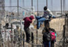 Is Washington Rewarding Illegal Hires? People climbing barbed wire fence wearing backpacks and hoodies