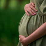 Pregnant person holding their belly in a green dress