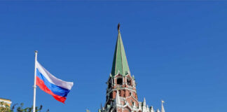 Russian flag and Kremlin tower against a clear blue sky