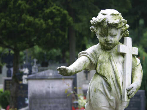 Weathered angel statue holding a cross in a cemetery