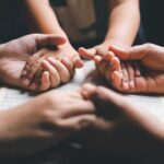 Multiple hands clasped together over an open book