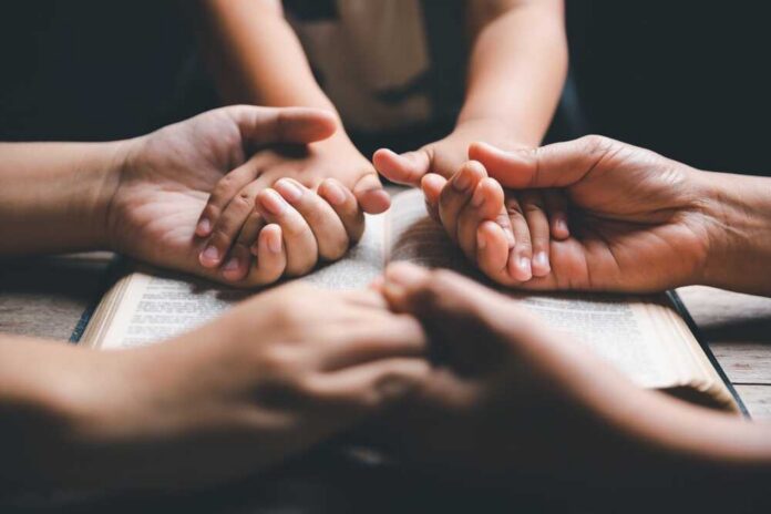 Multiple hands clasped together over an open book
