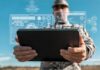 A soldier holding a tablet displaying digital data overlays