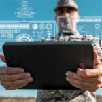A soldier holding a tablet displaying digital data overlays