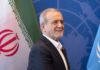 A man smiling in front of flags at a diplomatic event