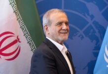 A man smiling in front of flags at a diplomatic event