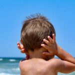 child with hands on ears facing the ocean