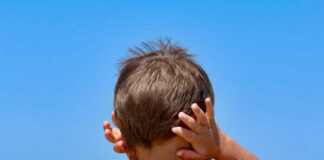 child with hands on ears facing the ocean