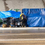 Prank Culture Crosses Line — Police Strike Two people at a sidewalk encampment with blue tarps and carts