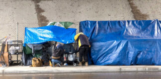 Two people at a sidewalk encampment with blue tarps and carts