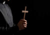 Priest Torches Pride Masses — Parish Backs Him Clergyperson holding a wooden cross