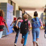 Children with backpacks running in a school corridor
