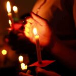 Twin Quakes Turn City Into Tomb Hands holding lit candles in a dark setting