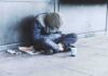 Person sitting on a sidewalk with head down and hood up