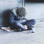 San Francisco Stunned: Homeless Man Down Person sitting on a sidewalk with head down and hood up
