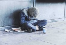 San Francisco Stunned: Homeless Man Down Person sitting on a sidewalk with head down and hood up