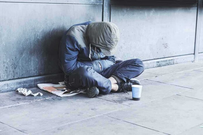 Person sitting on a sidewalk with head down and hood up