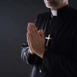 Clergyman in black robe praying with hands together