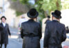 Gates, Guards… And It’s Getting Worse Two men in traditional black attire and hats walking down a street