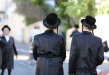 Gates, Guards… And It’s Getting Worse Two men in traditional black attire and hats walking down a street