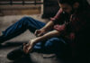 man sitting on floor injecting his arm with a syringe